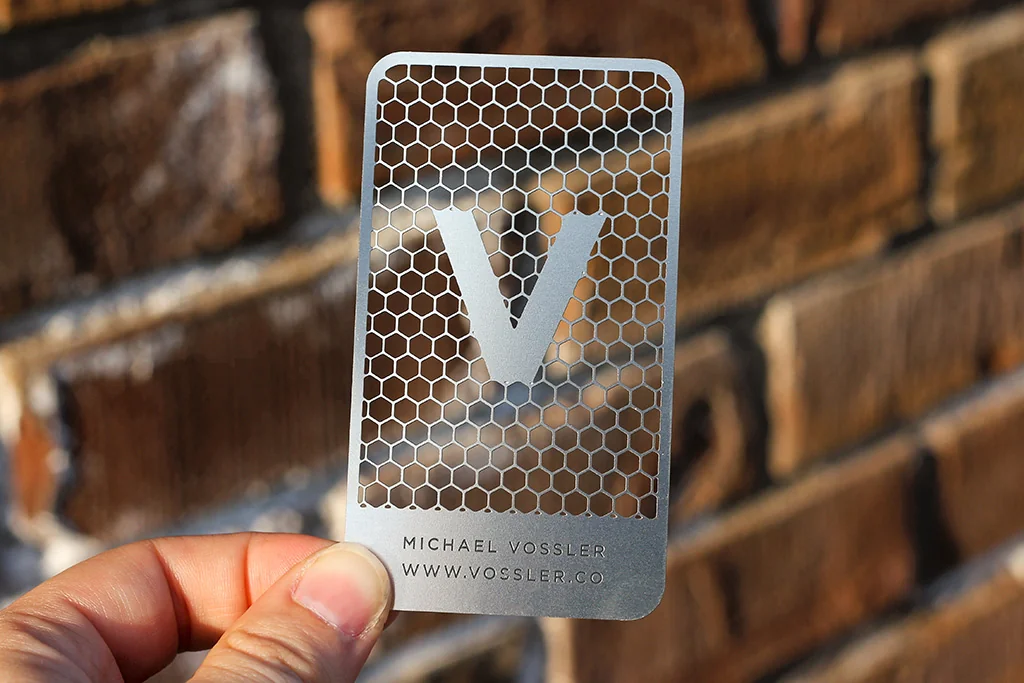 Product design example: hand holding a stainless steel card with intricate cutout monogram